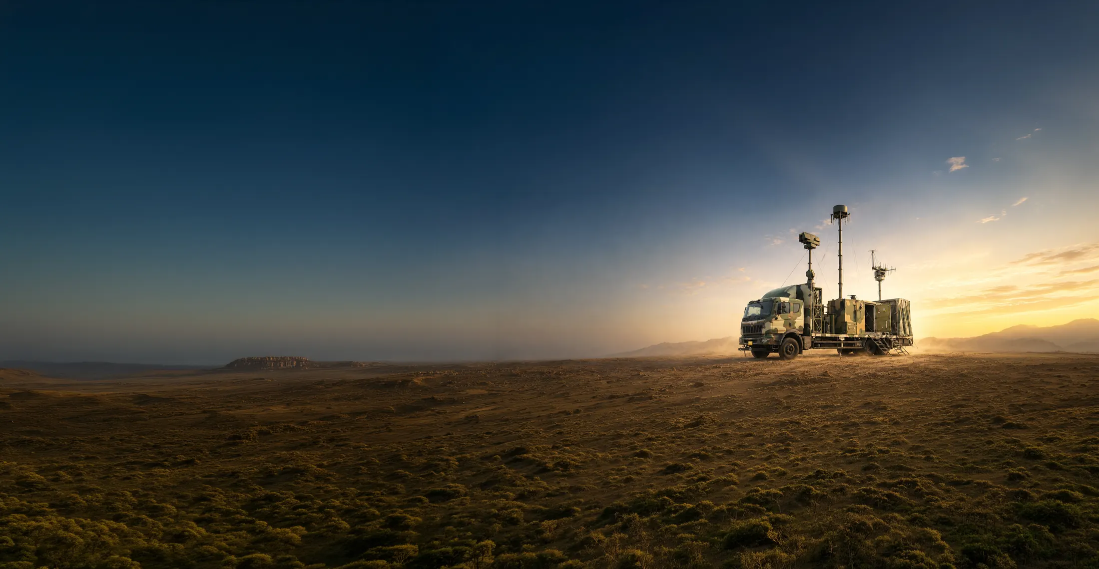 Zen Anti-Drone System deployed on open high ground at sunset: the containerised station on a truck with its sensor and antenna masts raised, mountains beyond.
