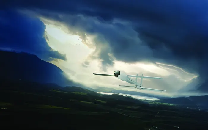 A fixed-wing Zen unmanned aerial vehicle in flight above a valley under storm cloud.