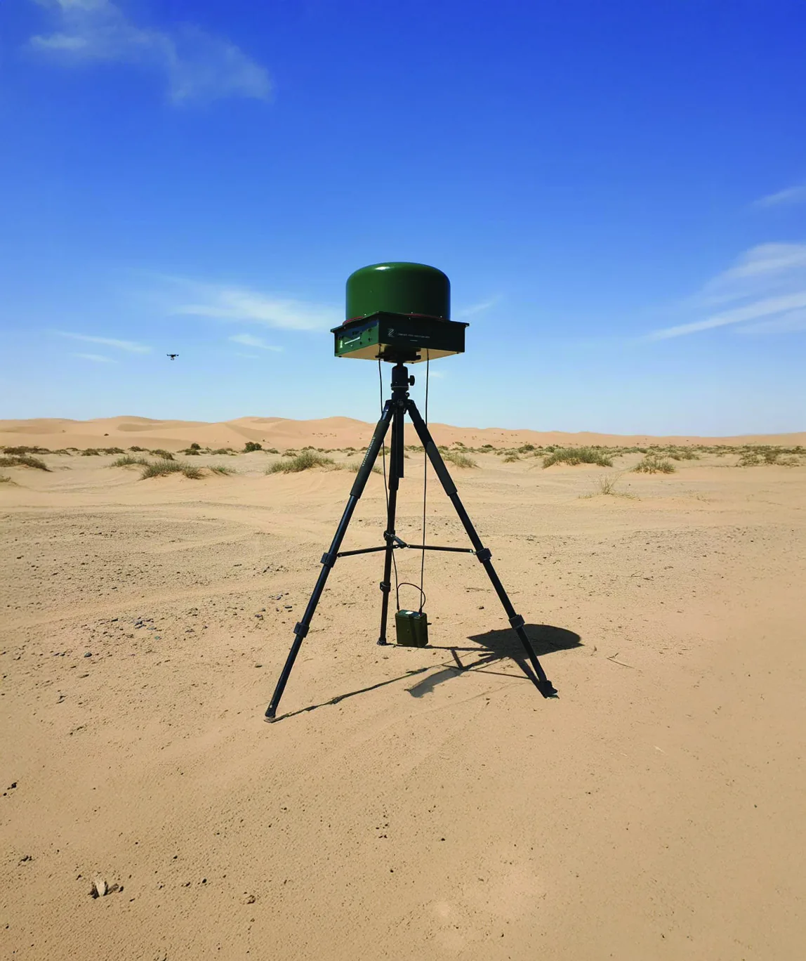 Zen RF-Based Drone Detector mounted on a tripod in open desert terrain, with a small drone visible in the sky at distance